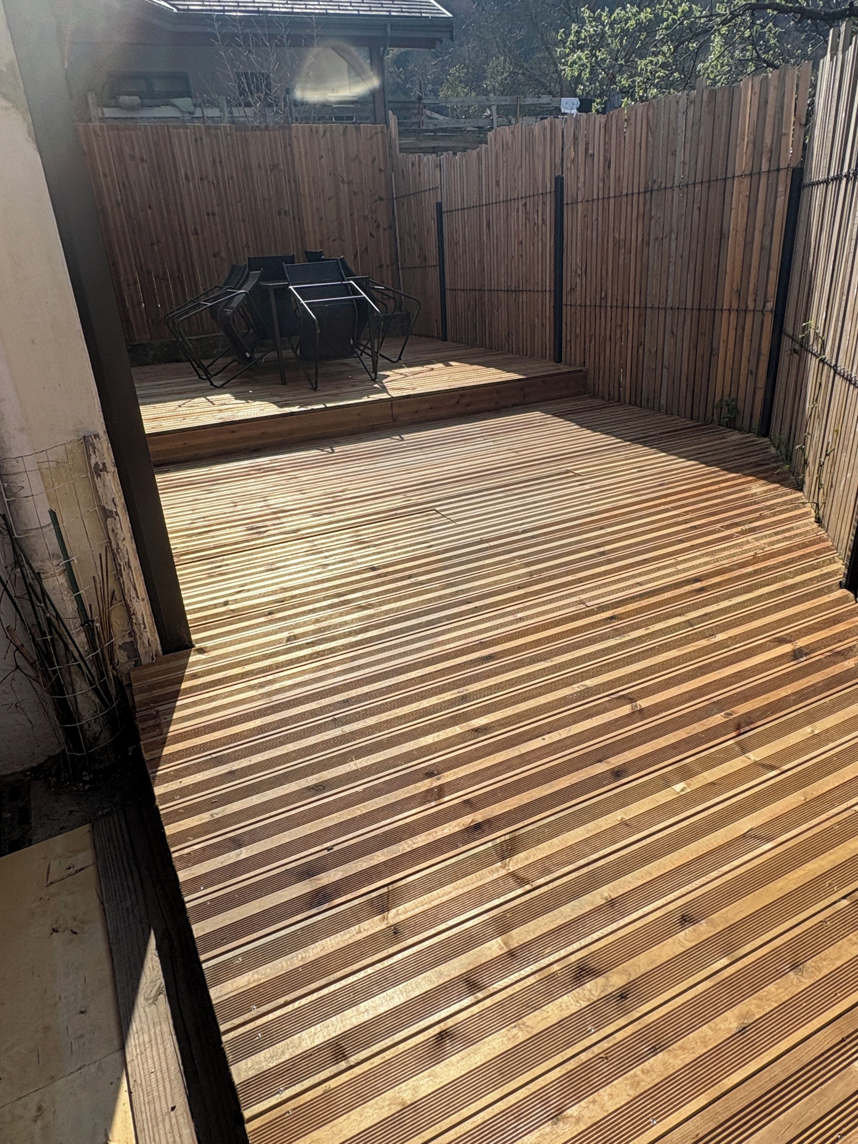 Un terrazzo in legno con tavolo e sedie in metallo, circondato da un recinto di legno.