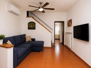 A living room with a sectional sofa, a ceiling fan, a mounted TV, and a staircase leading to another room. - Grande Giove – Spacious Family & Bike Home in the Heart of Finalborgo (Finale Ligure)
