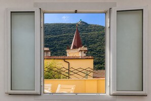 A window with a view of a mountain and a building with a red roof. - Grande Giove – Spacious Family & Bike Home in the Heart of Finalborgo (Finale Ligure)