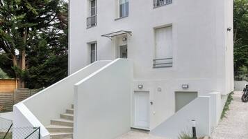 A modern two-story building with a staircase leading to the entrance, a covered outdoor area, and a vehicle parked nearby.