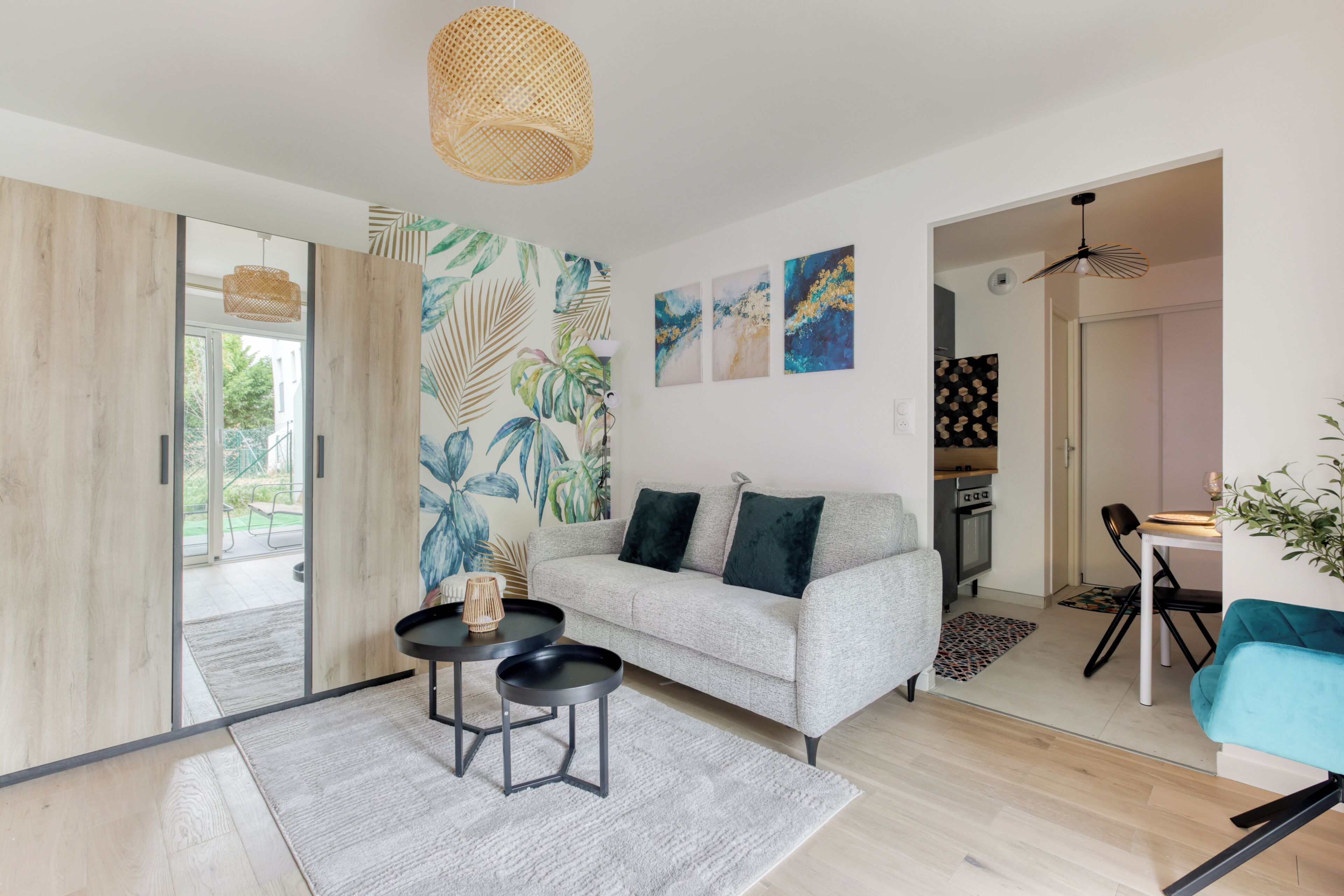 A modern living room with a grey sofa, a coffee table, and a dining area with a teal chair.