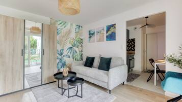 A modern living room with a grey sofa, a coffee table, and a dining area with a teal chair.