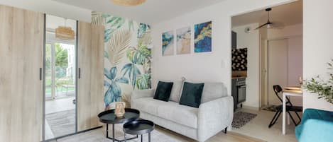 A modern living room with a grey sofa, a coffee table, and a dining area with a teal chair.