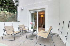 Terrassa exterior amb taula de vidre i quatre cadires, una planta en test i una làmpada penjant.