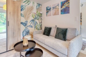 A modern living room with a sofa, a round table, and a decorative wall with leaf patterns. - L'Écrin Vert — Chic Studio & Private Terrace (Rueil-Malmaison)