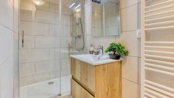 A modern bathroom with a glass shower enclosure, a wooden vanity with a sink, and a potted plant.