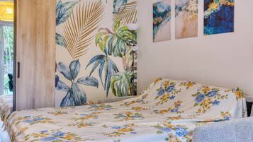 A bedroom with a bed, a wall with a tropical leaf pattern, and three abstract paintings.