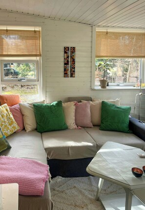 A cozy living room with a sectional sofa, a coffee table, and a window with blinds. - Summer house with wild garden by Arresø (Frederiksværk)