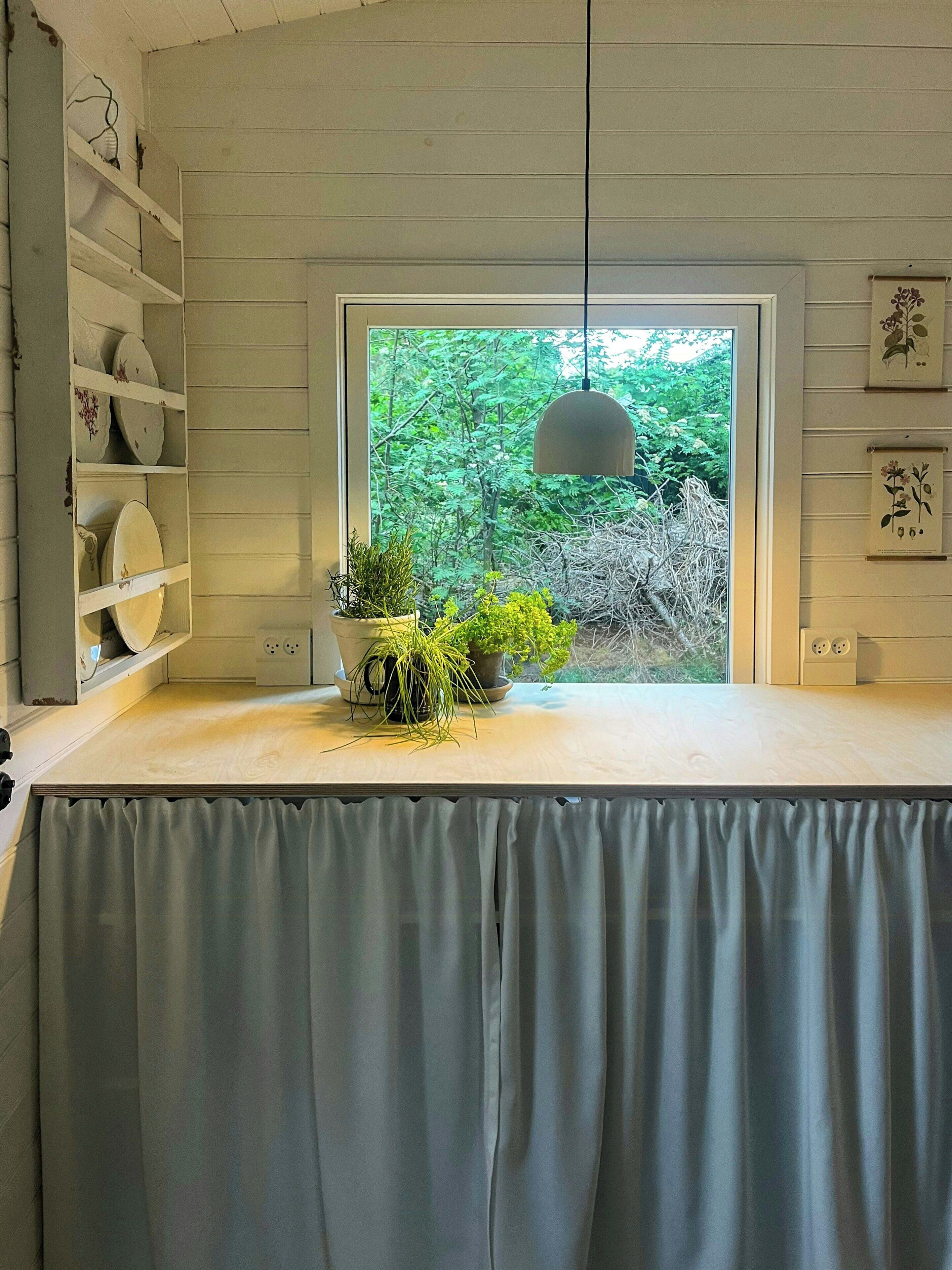 A kitchen with a window, shelves with dishes, and a hanging light fixture.