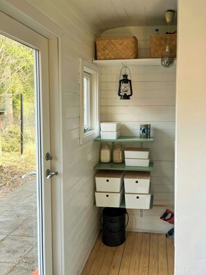 A storage area with shelves, a lantern, and a door leading outside. - Summer house with wild garden by Arresø (Frederiksværk)