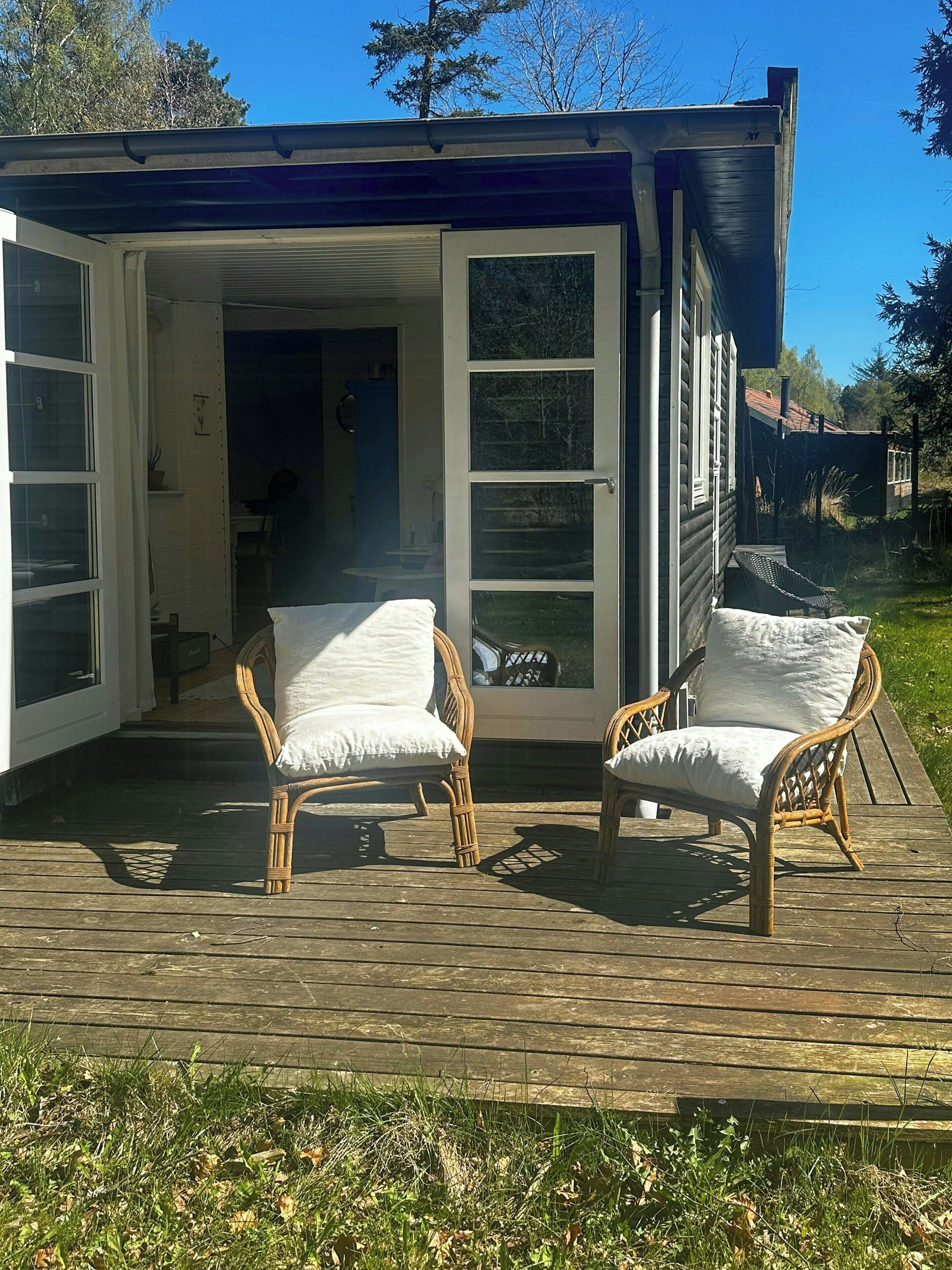 A wooden deck with two wicker chairs and a white door leading to an interior space.