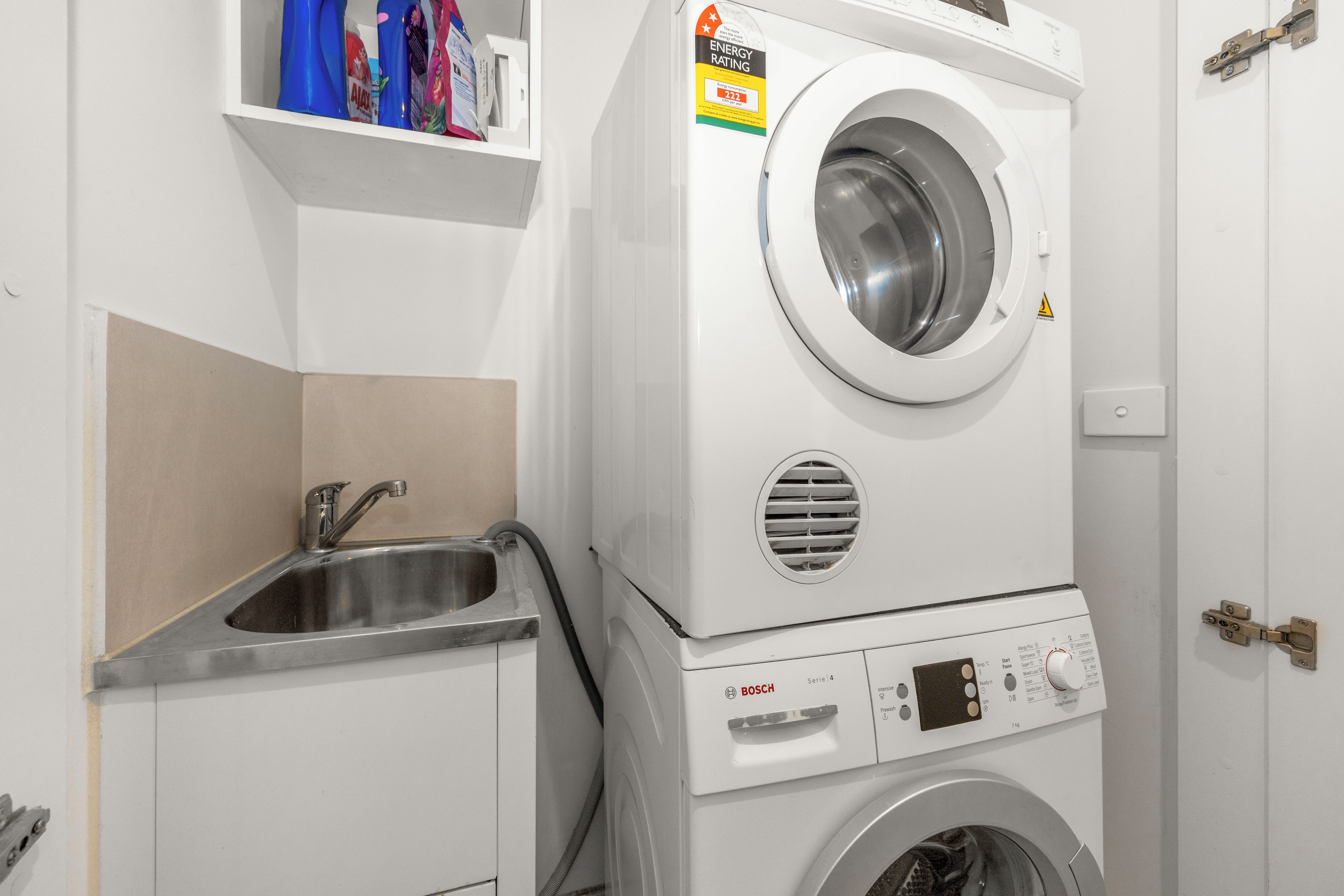 Un appareil combiné lave-linge et sèche-linge, avec un panneau de commande, un évier et une étagère au-dessus de l’appareil.