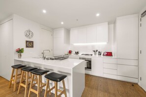 Cozinha moderna com ilha central, banquetas de bar e armários brancos.