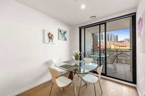 Eine moderne Wohnung mit einem Glastisch, weißen Stühlen und einem Balkon mit Stadtblick.