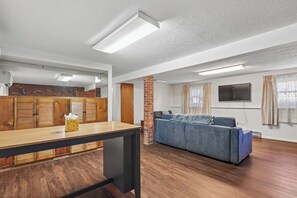 Ein geräumiger Wohnbereich mit Holzboden, einem blauen Sofa, einem Holztisch und einer Ziegelstütze.