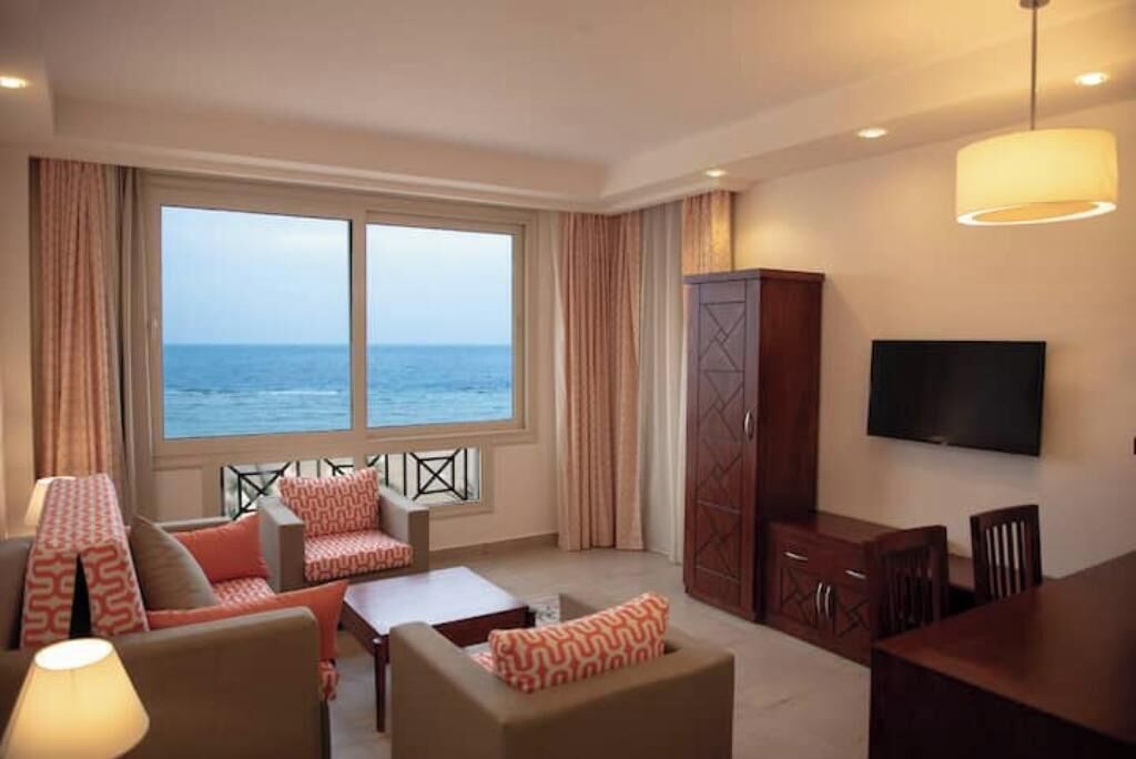 Quarto de hotel com uma janela grande, televisão de tela plana, área de refeições e um guarda-roupa.