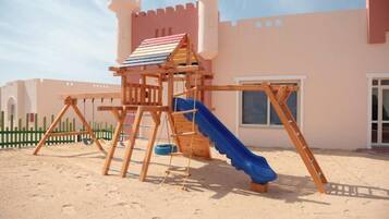 Una estructura de madera con un tobogán, una escalera de cuerda y una torre con forma de castillo.