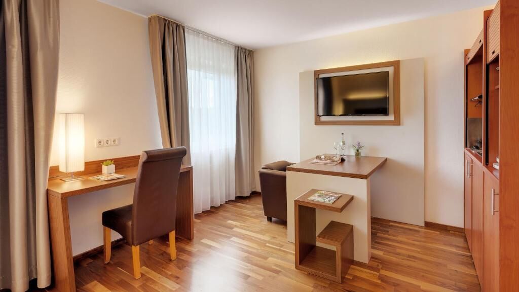 Ein Hotelzimmer mit Schreibtisch, Stuhl, Fernseher und einem kleinen Schrank.