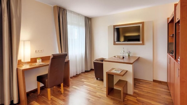 A hotel room with a desk, chair, TV, and a small cabinet.