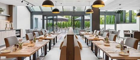 Un comedor moderno con mesas largas, sillas e iluminación colgante.