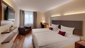 Een hotelkamer met twee bedden, een aan de muur bevestigde televisie, een bureau en een stoel.