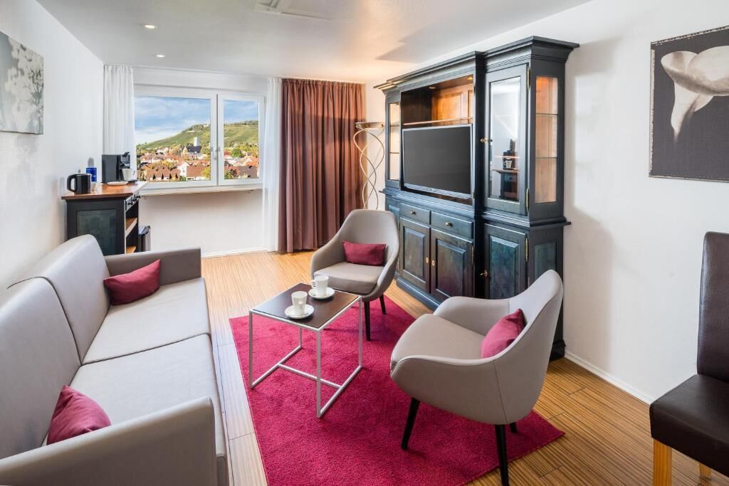 Ein modernes Wohnzimmer mit einer Couch, zwei Sesseln, einem Couchtisch und einem Schrank mit Fernseher.
