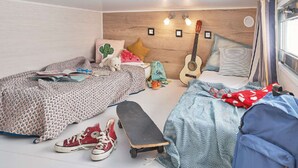 Quarto com duas camas, um violão, um skate e diversos objetos pessoais.