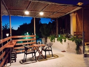 Zona de pati exterior amb taula i cadires, teulada de palla i vista del paisatge circumdant.