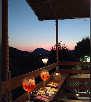 Una terrassa amb vistes al capvespre, una taula amb begudes i aperitius, i una làmpada.