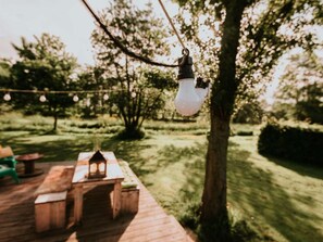 An outdoor deck with a wooden table and benches, surrounded by trees and greenery. - Kampari - Tiny house - Praathuis by Interhome (Delfstrahuizen)