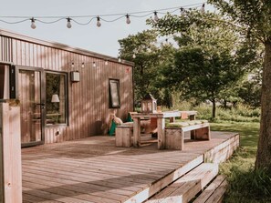 A wooden deck with a table and benches, surrounded by trees. - Kampari - Tiny house - Praathuis by Interhome (Delfstrahuizen)