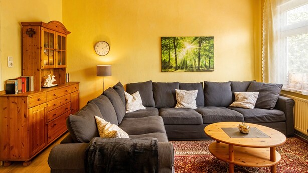 A living room with a sectional sofa, a wooden cabinet, a round coffee table, and a painting of a forest.