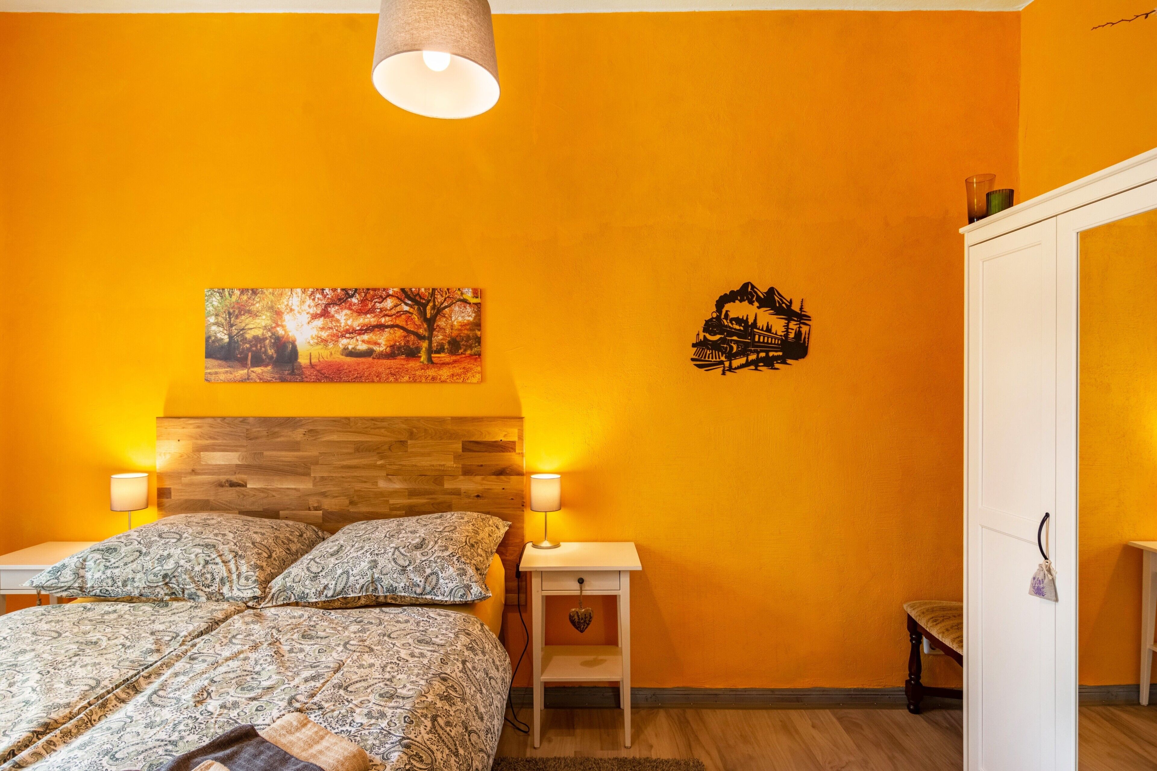Un dormitori amb llit, tauletes de nit, làmpada, quadre i un adhesiu mural.