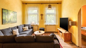 A living room with a sofa, a coffee table, a TV, and a cross on the wall.