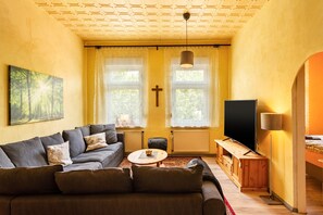 Ein Wohnzimmer mit einer Couch, einem Couchtisch, einem Fernseher und einem Kreuz an der Wand.