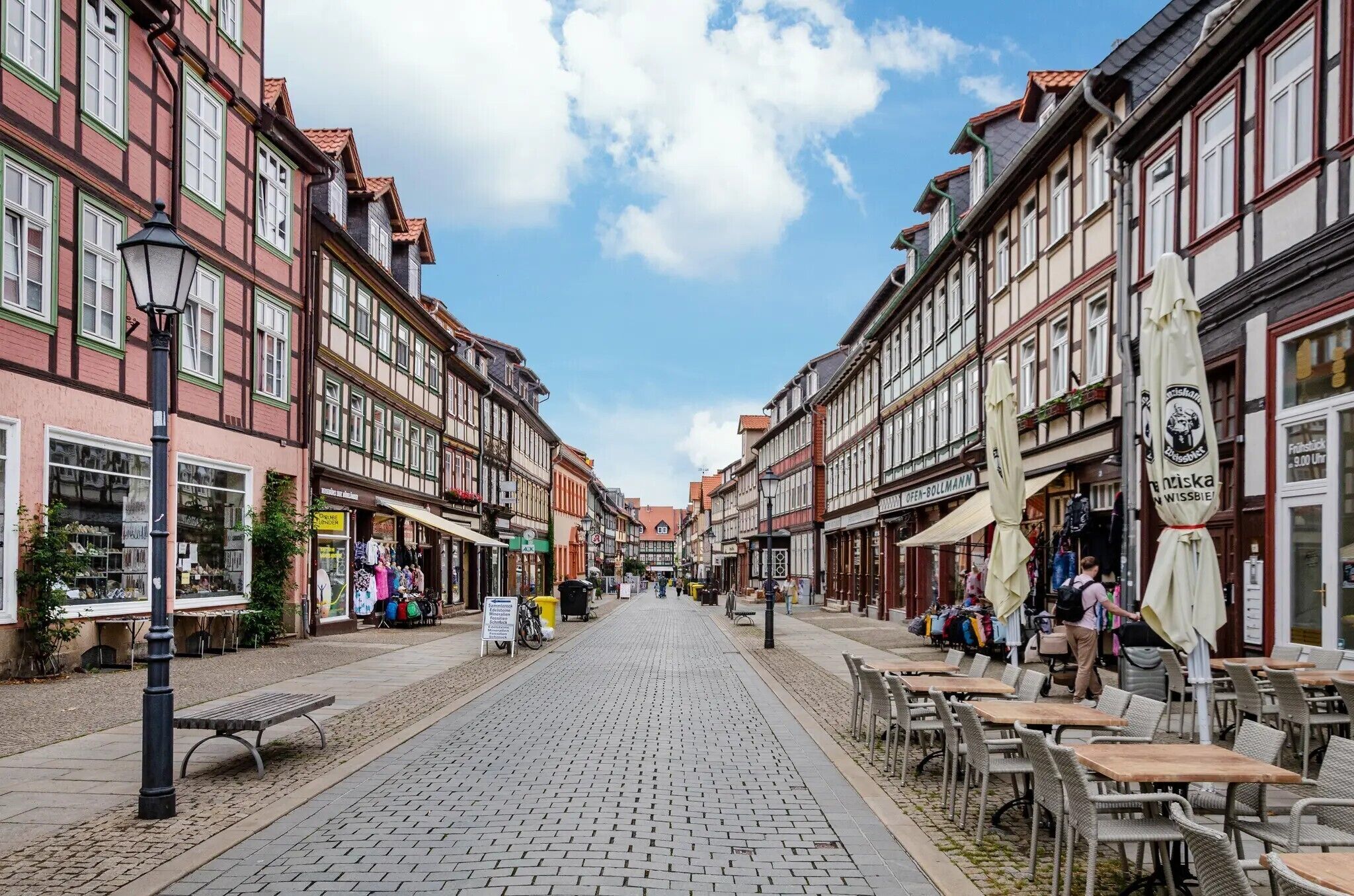 A cobblestone street lined with traditional half-timbered buildings, outdoor seating, and a clear sky.