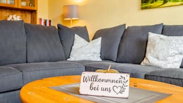 Ein Wohnzimmer mit grauem Sofa, einem Holztisch und einem Willkommensschild.