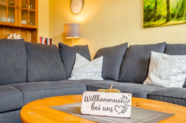 A living room with a grey sofa, a wooden coffee table, and a welcome sign.