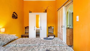 A bedroom with two beds, a white wardrobe, a wooden chair, and a small table with a vase of flowers.