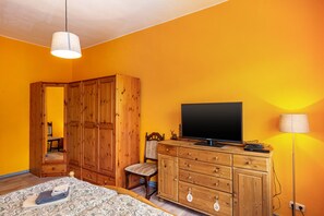 A bedroom with a bed, wooden wardrobe, television, and a lamp.