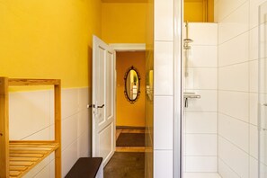 Ein Badezimmer mit weißen Fliesen, einer Dusche und einer hölzernen Sitzbank.