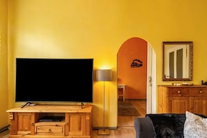 A living room with a large flat-screen TV, wooden entertainment unit, and a lamp.
