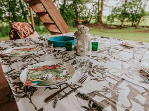 An outdoor dining table with a floral tablecloth, plates, cutlery, and a lantern. - Kampari - Luxe Safaritent - De Jungle by Interhome (Delfstrahuizen)