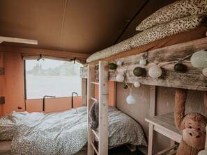 A bunk bed with a patterned blanket, a teddy bear, and a view of a snowy landscape. - Kampari - Luxe Safaritent - De Jungle by Interhome (Delfstrahuizen)