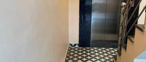 A hallway with a patterned floor leading to a metallic elevator.