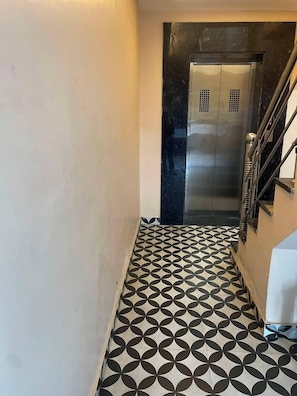 A hallway with a patterned floor leading to a metallic elevator. - Hotel Mehman  (Ajmer)