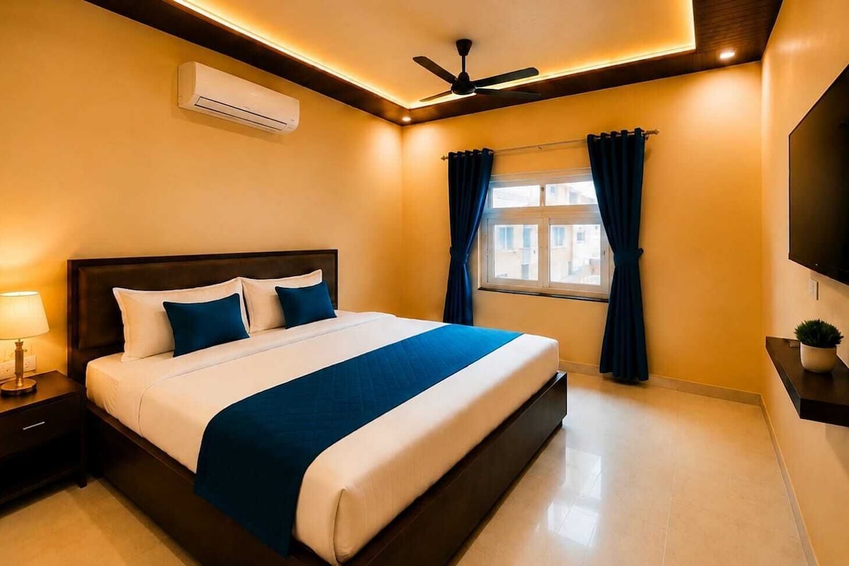 Hotelkamer met een bed, nachtkastje, airconditioning, plafondventilator, raam met gordijnen en een flatscreen televisie aan de muur bevestigd.