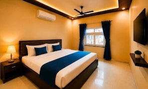 Hotelkamer met een bed, nachtkastje, airconditioning, plafondventilator, raam met gordijnen en een flatscreen televisie aan de muur bevestigd.