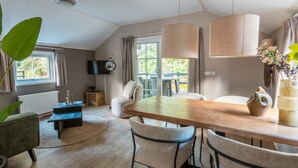 Uma sala de estar moderna com uma mesa de jantar de madeira, assentos confortáveis, uma TV de tela plana e uma grande janela com cortinas.