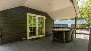 Área externa coberta com deck de madeira, mesa com cadeiras e porta que dá para um alpendre.